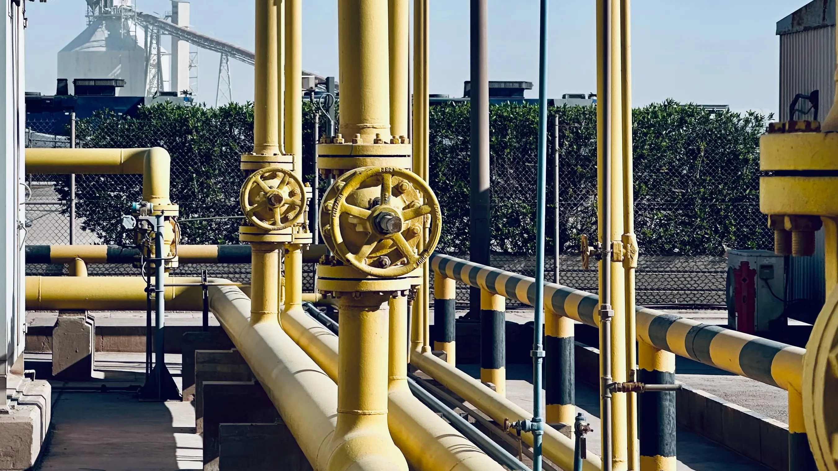 Yellow gas pipework and hand-wheel valves on an outdoor pipe rack at a gas facility.